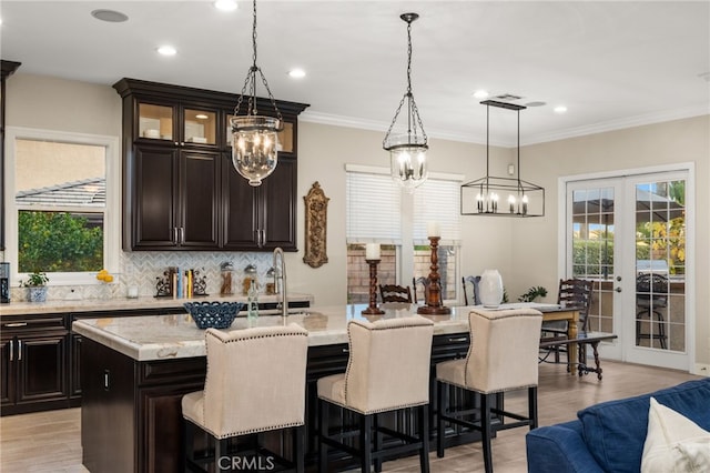 kitchen featuring pendant lighting, french doors, a center island with sink, light wood-type flooring, and ornamental molding