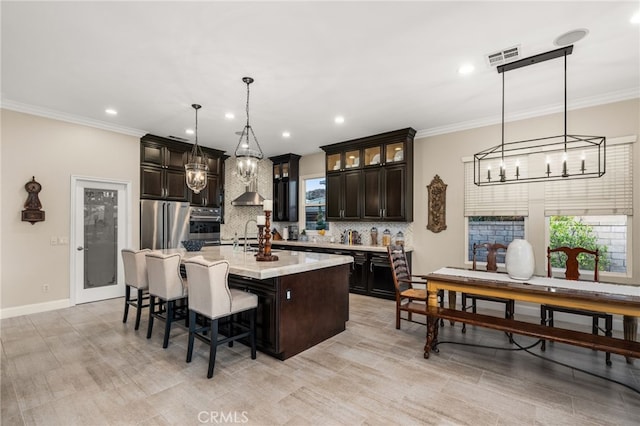 kitchen featuring a breakfast bar, hanging light fixtures, an island with sink, tasteful backsplash, and dark brown cabinetry