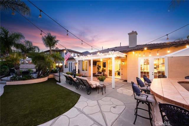 back house at dusk featuring a pergola, a yard, and an outdoor bar