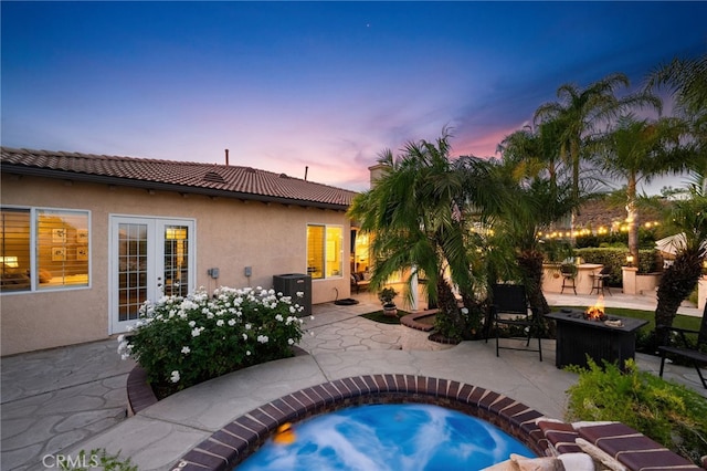 pool at dusk with a fire pit, a patio area, french doors, and a hot tub