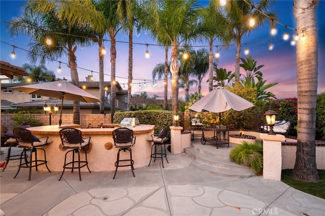 patio terrace at dusk featuring exterior bar, an outdoor kitchen, and area for grilling