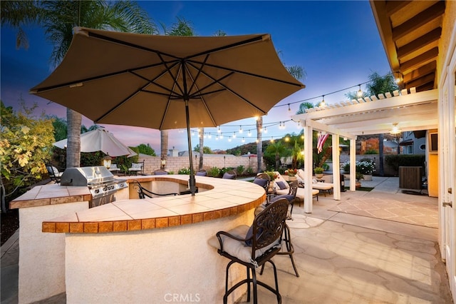 patio terrace at dusk featuring an outdoor kitchen, area for grilling, and a pergola