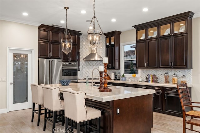 kitchen featuring tasteful backsplash, a center island with sink, stainless steel appliances, and decorative light fixtures