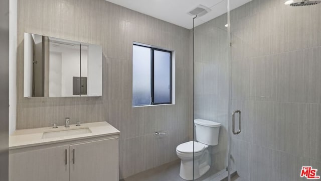 bathroom with vanity, toilet, tile walls, and a shower with shower door