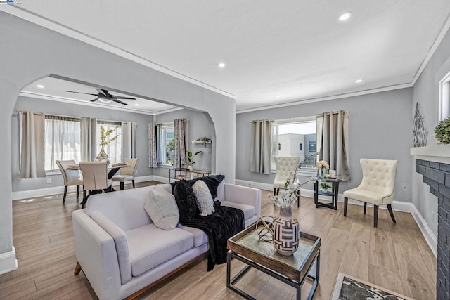 living room featuring a fireplace, light hardwood / wood-style flooring, ceiling fan, and crown molding