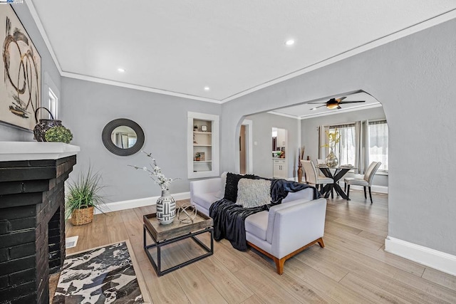 living room with light wood-type flooring, a brick fireplace, ceiling fan, and crown molding