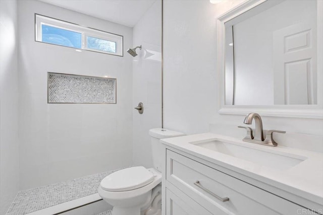 bathroom featuring a tile shower, vanity, and toilet