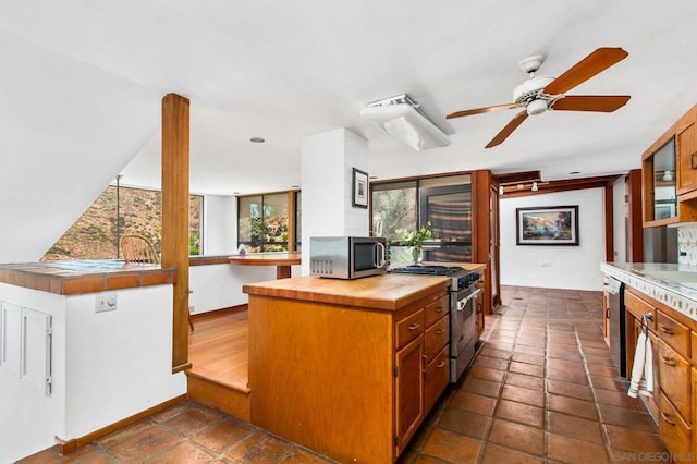 kitchen with stainless steel appliances, wooden counters, ceiling fan, and dark tile patterned flooring