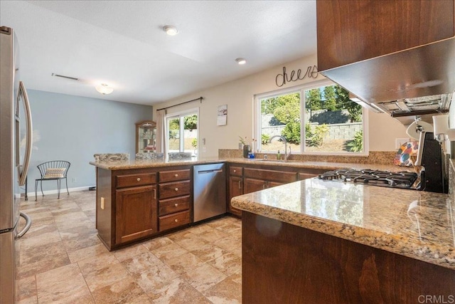 kitchen with kitchen peninsula, light stone counters, stainless steel appliances, exhaust hood, and sink