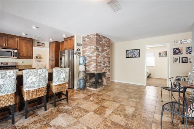 kitchen with a fireplace, appliances with stainless steel finishes, light stone counters, and a kitchen breakfast bar