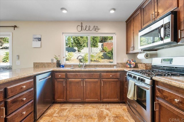 kitchen featuring kitchen peninsula, stainless steel appliances, light stone counters, and sink