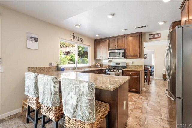 kitchen featuring a kitchen bar, kitchen peninsula, light stone countertops, and appliances with stainless steel finishes