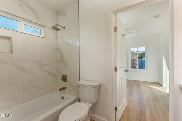 bathroom with wood-type flooring, toilet, tiled shower / bath combo, and a wealth of natural light