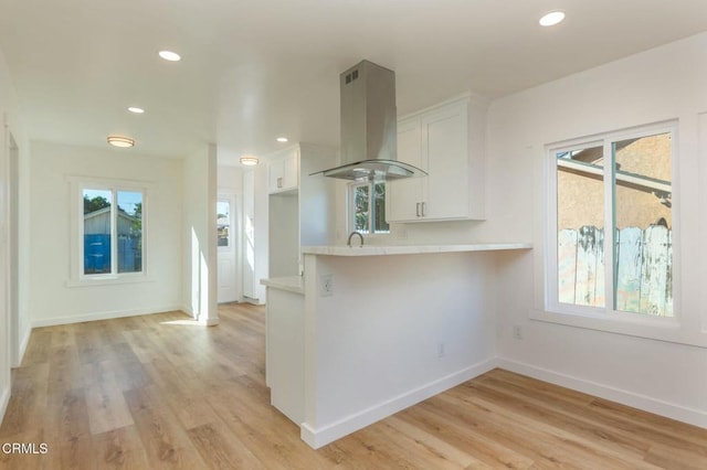 kitchen featuring white cabinetry, island exhaust hood, kitchen peninsula, and light hardwood / wood-style flooring