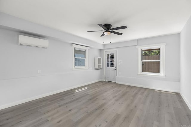 spare room with light wood-type flooring, a wall mounted AC, and ceiling fan