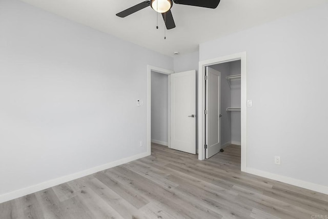 unfurnished bedroom featuring ceiling fan, light wood-type flooring, a walk in closet, and a closet