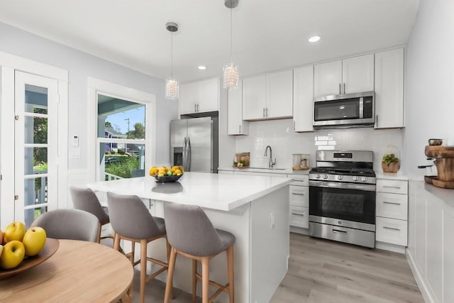 kitchen featuring white cabinets, pendant lighting, appliances with stainless steel finishes, and light hardwood / wood-style flooring