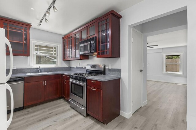 kitchen featuring appliances with stainless steel finishes, light wood-type flooring, track lighting, ceiling fan, and sink