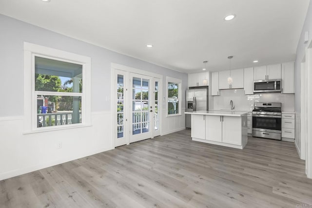 kitchen with appliances with stainless steel finishes, light hardwood / wood-style flooring, a kitchen island, and hanging light fixtures