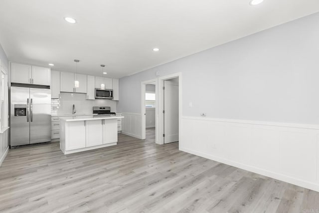 kitchen with stainless steel appliances, pendant lighting, light hardwood / wood-style flooring, white cabinets, and a center island