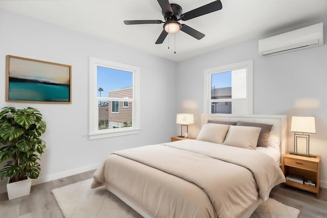 bedroom with multiple windows, light wood-type flooring, a wall mounted AC, and ceiling fan