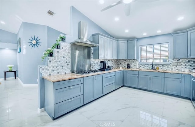 kitchen with decorative backsplash, vaulted ceiling, stainless steel gas cooktop, sink, and wall chimney range hood