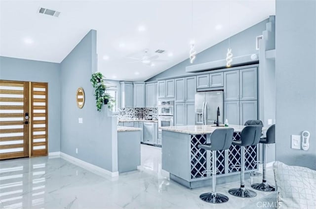 kitchen featuring gray cabinetry, lofted ceiling, light stone counters, kitchen peninsula, and stainless steel appliances