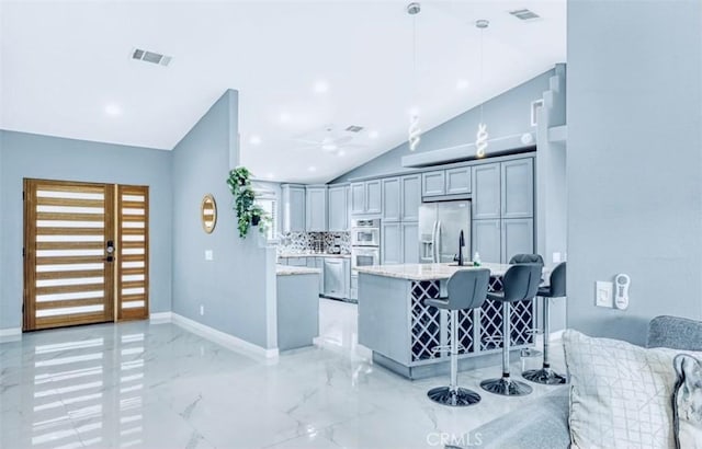 kitchen with gray cabinetry, lofted ceiling, light stone countertops, decorative light fixtures, and stainless steel appliances