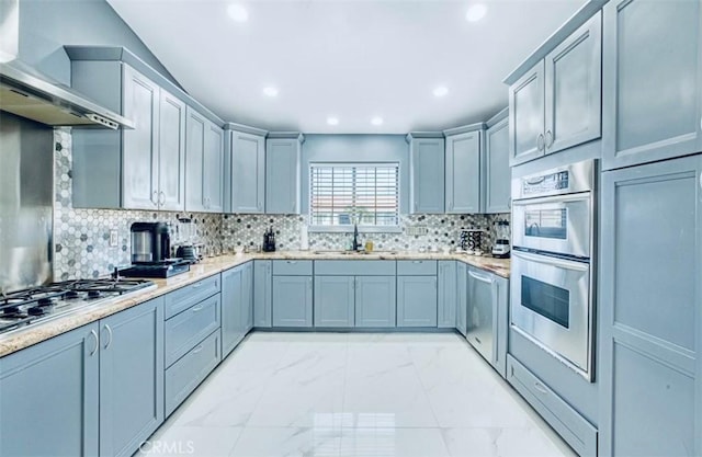 kitchen with decorative backsplash, appliances with stainless steel finishes, wall chimney exhaust hood, sink, and gray cabinets