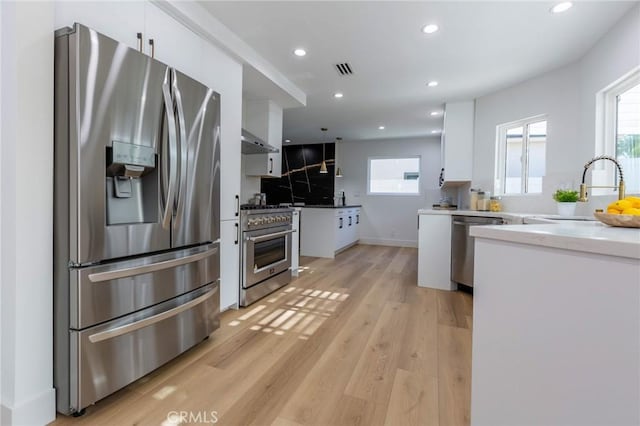 kitchen with light wood-type flooring, stainless steel appliances, exhaust hood, sink, and white cabinetry