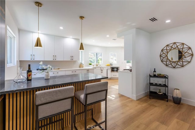 kitchen with kitchen peninsula, a kitchen breakfast bar, light hardwood / wood-style floors, white cabinetry, and hanging light fixtures