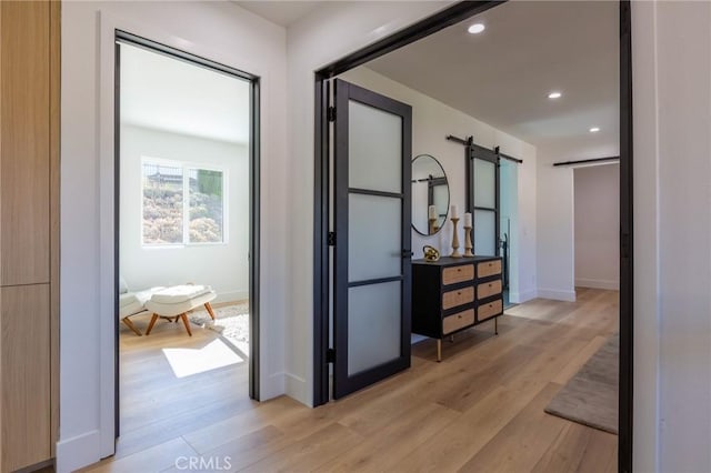 hall with a barn door and light hardwood / wood-style flooring