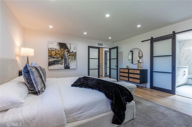 bedroom featuring a barn door, ensuite bathroom, and hardwood / wood-style flooring