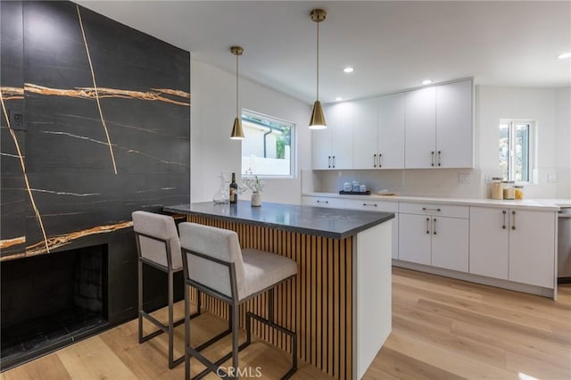 kitchen featuring backsplash, light wood-type flooring, decorative light fixtures, a kitchen bar, and white cabinetry