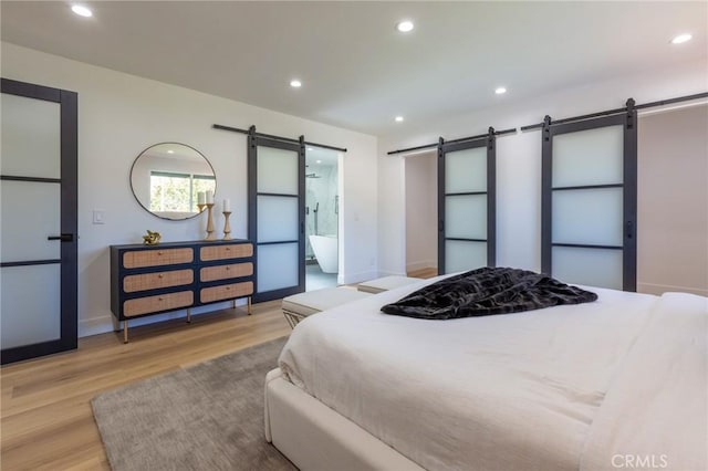 bedroom featuring connected bathroom, light hardwood / wood-style floors, and a barn door