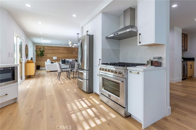 kitchen with white cabinetry, wall chimney range hood, appliances with stainless steel finishes, and light hardwood / wood-style flooring