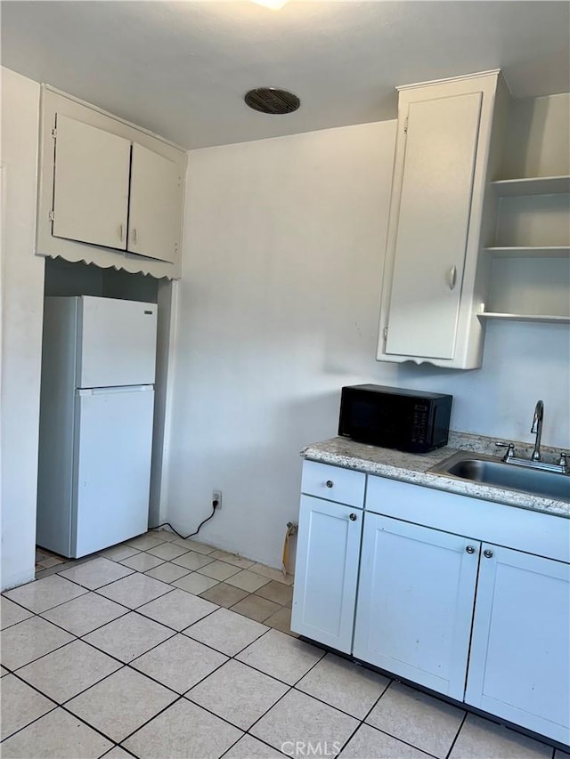 kitchen with light tile patterned floors, white refrigerator, white cabinetry, and sink