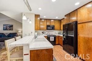 kitchen with sink, kitchen peninsula, vaulted ceiling, black appliances, and light wood-type flooring