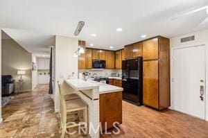 kitchen with black appliances, a kitchen breakfast bar, hanging light fixtures, light hardwood / wood-style floors, and kitchen peninsula