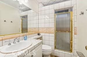 bathroom with toilet, an enclosed shower, tile walls, and vanity