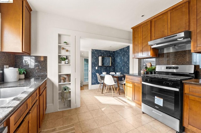 kitchen featuring backsplash, sink, built in features, dark stone countertops, and stainless steel gas stove