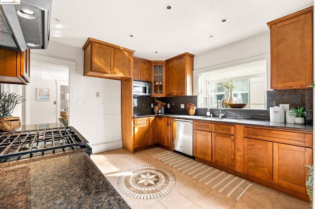 kitchen featuring sink, stainless steel appliances, dark stone counters, decorative backsplash, and light tile patterned flooring