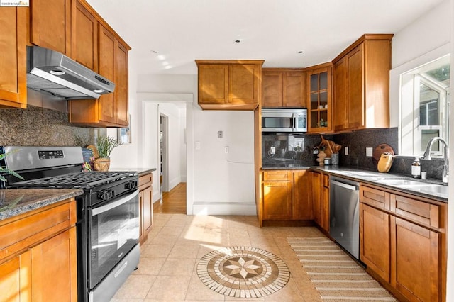 kitchen featuring dark stone counters, sink, decorative backsplash, light tile patterned floors, and appliances with stainless steel finishes