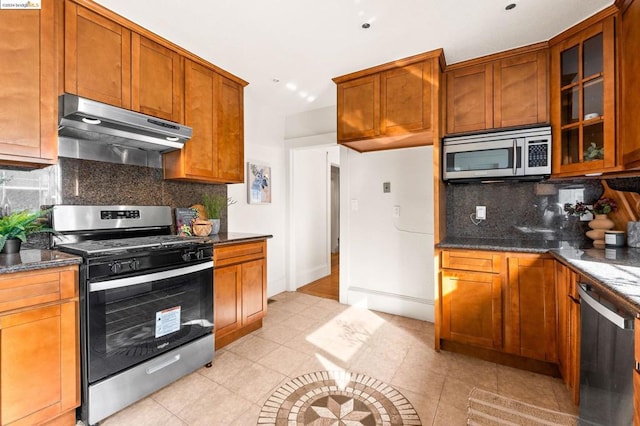 kitchen featuring dark stone counters, decorative backsplash, light tile patterned floors, and stainless steel appliances