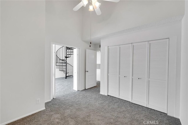 unfurnished bedroom with ceiling fan, carpet floors, a closet, and a high ceiling