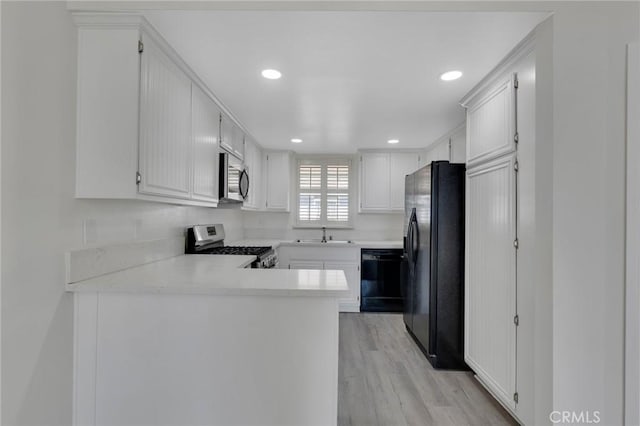 kitchen with black appliances, sink, white cabinets, kitchen peninsula, and light hardwood / wood-style flooring