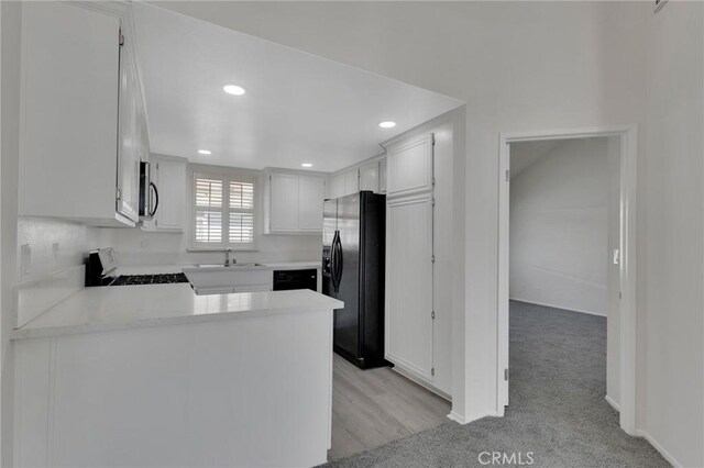 kitchen featuring light carpet, kitchen peninsula, white cabinets, and black appliances