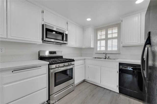 kitchen with stainless steel appliances, white cabinetry, sink, and light hardwood / wood-style flooring