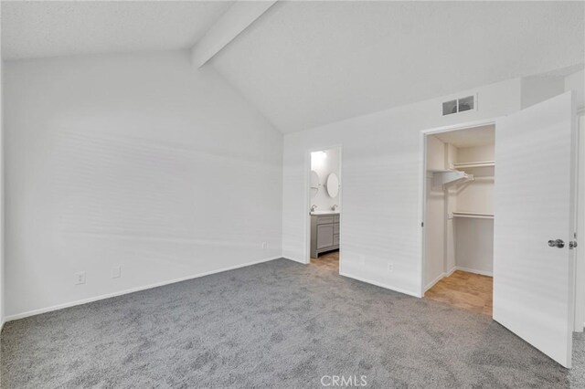 unfurnished bedroom with a walk in closet, connected bathroom, carpet flooring, and lofted ceiling with beams