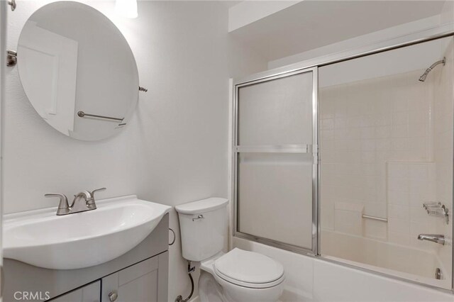 full bathroom featuring vanity, combined bath / shower with glass door, and toilet